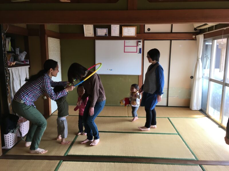 畳の部屋で、親子がフラフープを門に見立てて遊んでいる様子