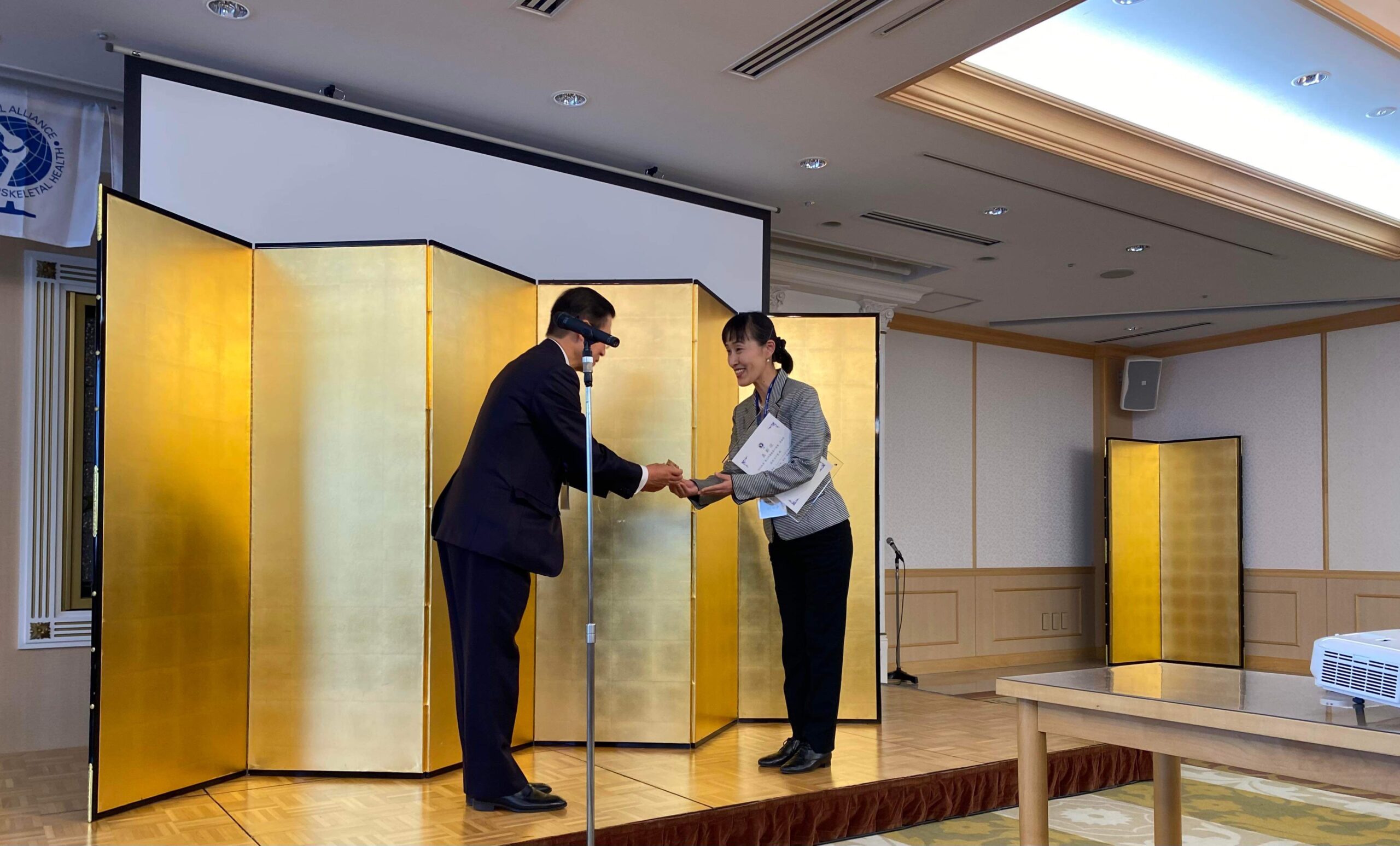 成田が壇上で、運動器の健康・日本協会の理事長より表彰を受ける様子。