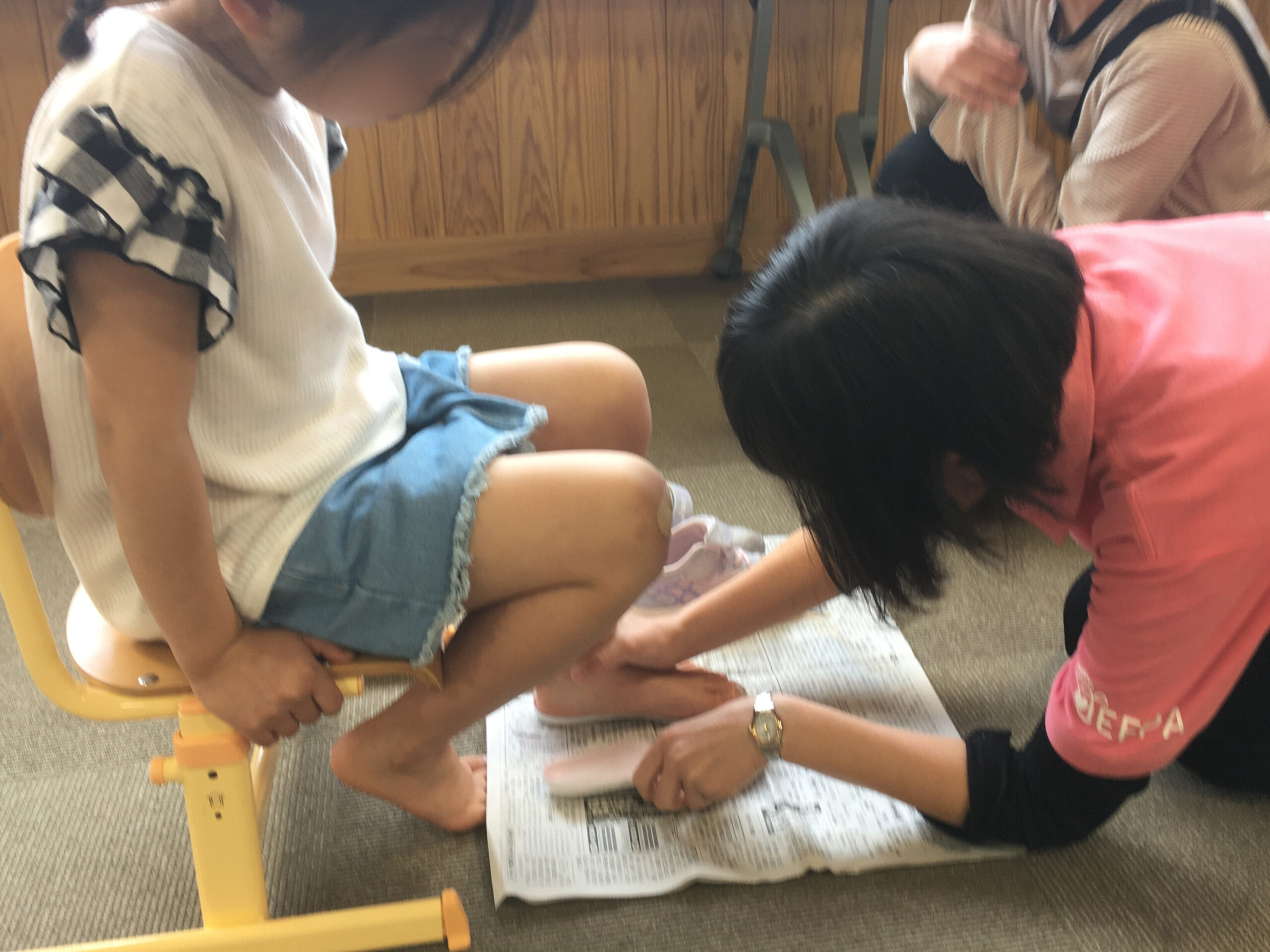 中敷きを使った靴のサイズチェックの方法を教える足育アドバイザーの成田。子どもも興味深そうに足もとを見つめている。