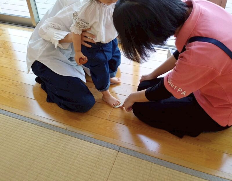 子どもを靴の中敷きの上に立たせて、サイズが合っているかを確認している場面。保護者がそばで見守っている(2025年5月8日、かのう子育て交流ひろば)