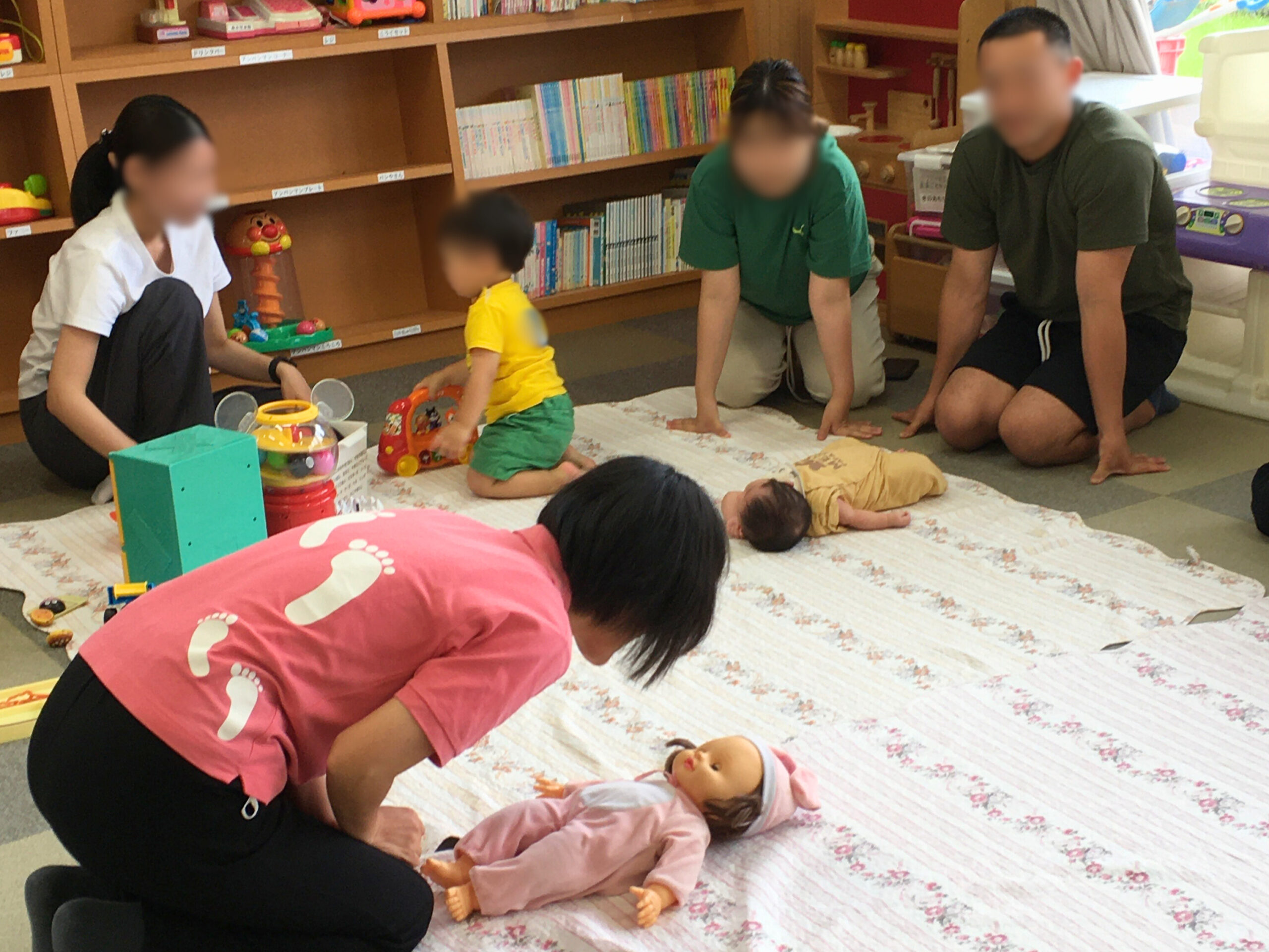 生後すぐの赤ちゃんにもできる関わりの工夫「正面からやさしく声をかける」を、赤ちゃん人形を使って説明する講師と、それを真剣に見る両親の姿。(2025年5月29日)