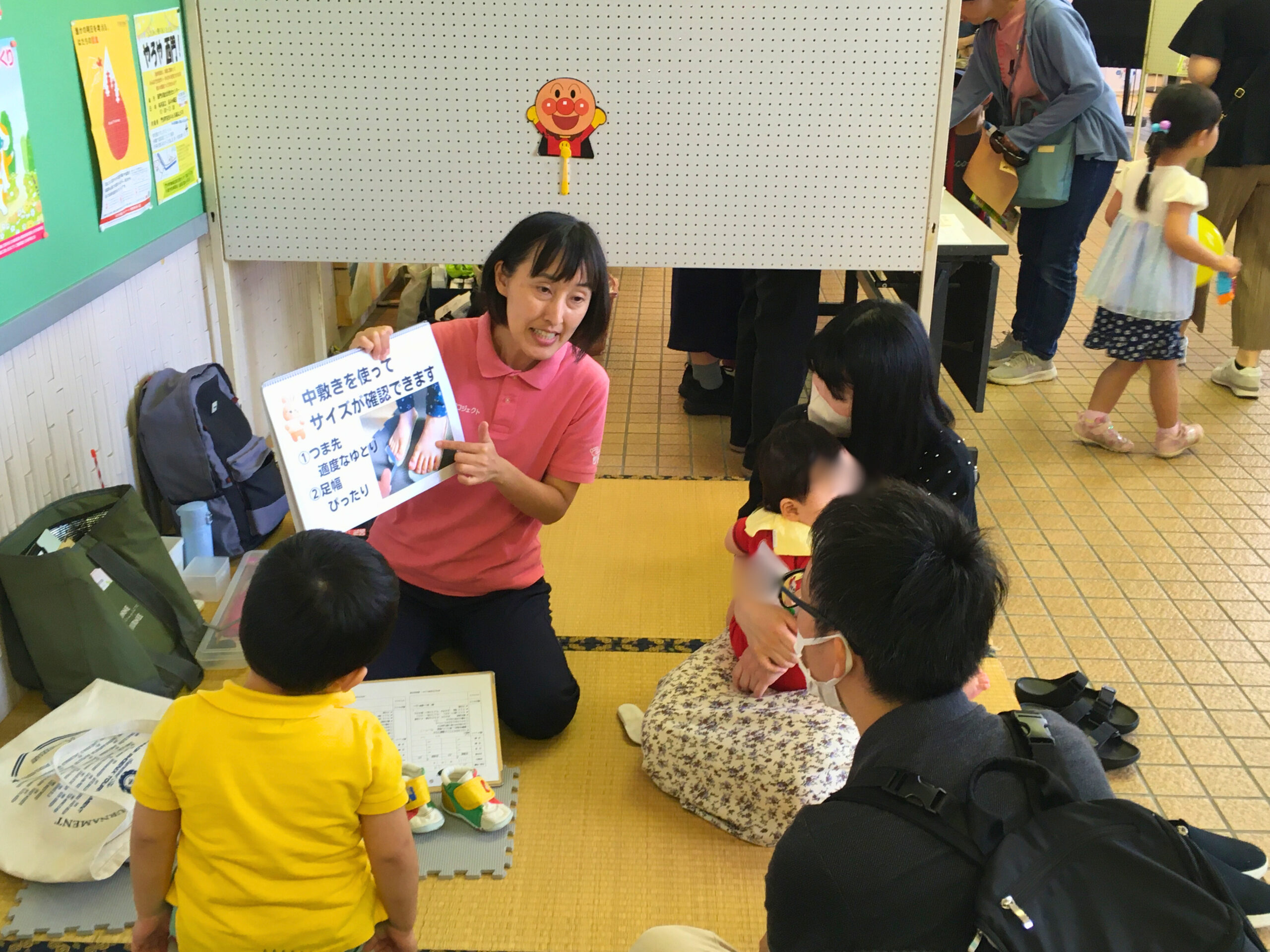 中敷きを使ったサイズチェックの方法を説明する講師と、それを聞く両親と子どもの様子(2025年6月1日 門川町子育て応援フェスティバル)