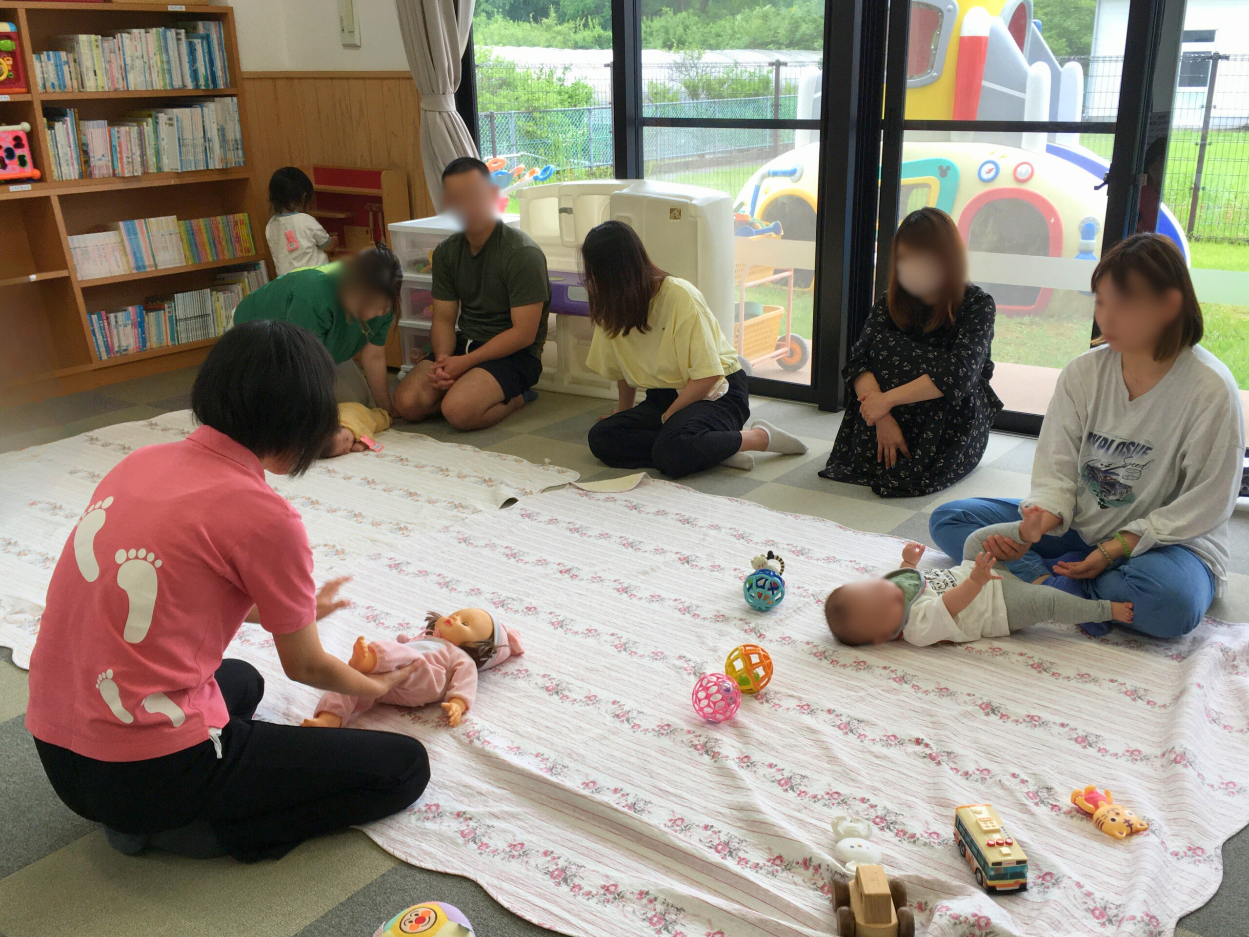 「はいはいの足に左右差がある」という悩みに応え、股関節の柔軟性を高める動きを取り入れた遊びを、赤ちゃん人形で実演する講師。それを見守る、赤ちゃんを育てる親たちの姿。(2025年5月29日)
