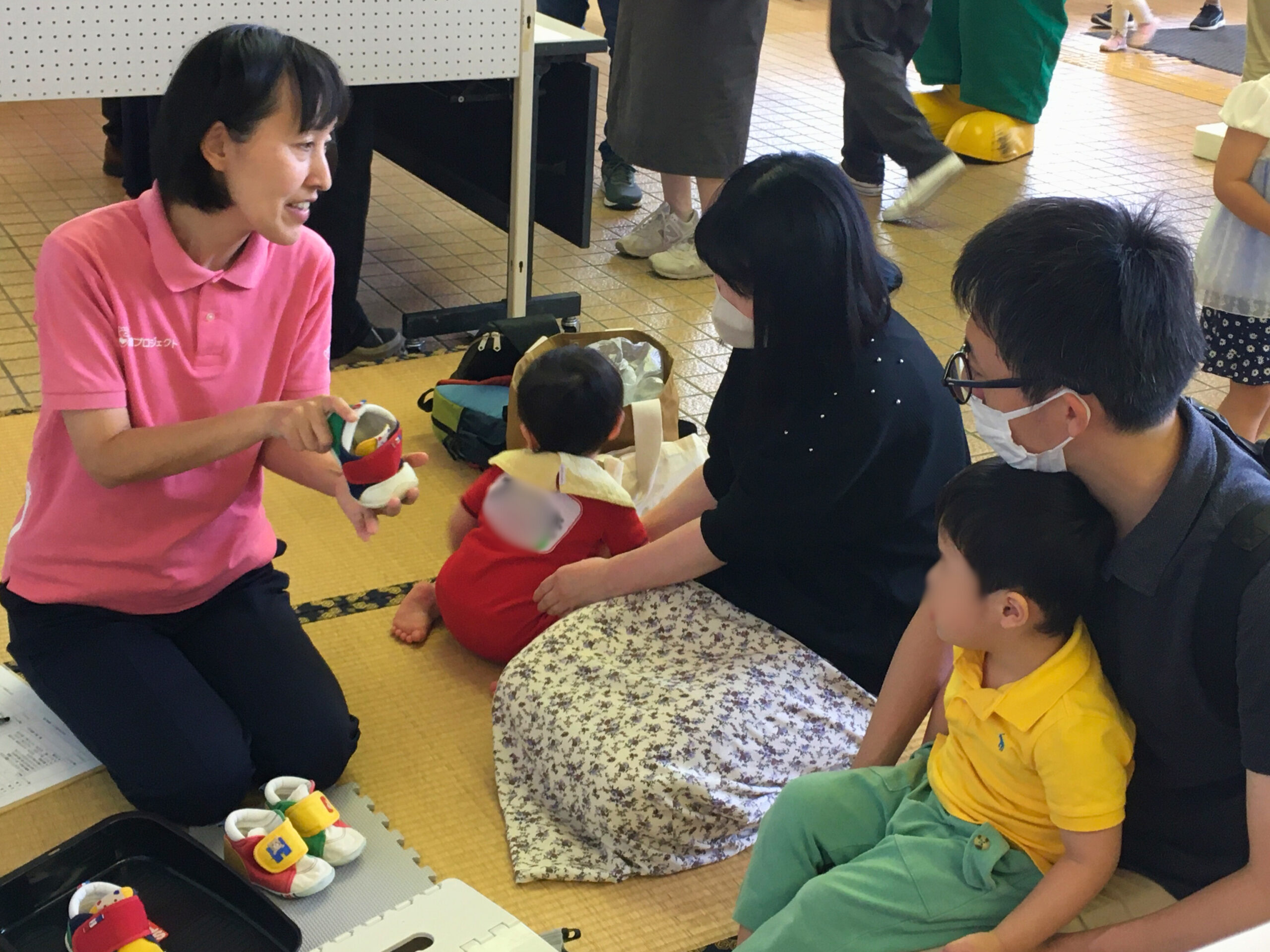 足育ブースで、赤ちゃん用の靴を手に取り、靴の選び方を説明している講師と、熱心に聞く親子の様子(2025年6月1日 門川町子育て応援フェスティバル)